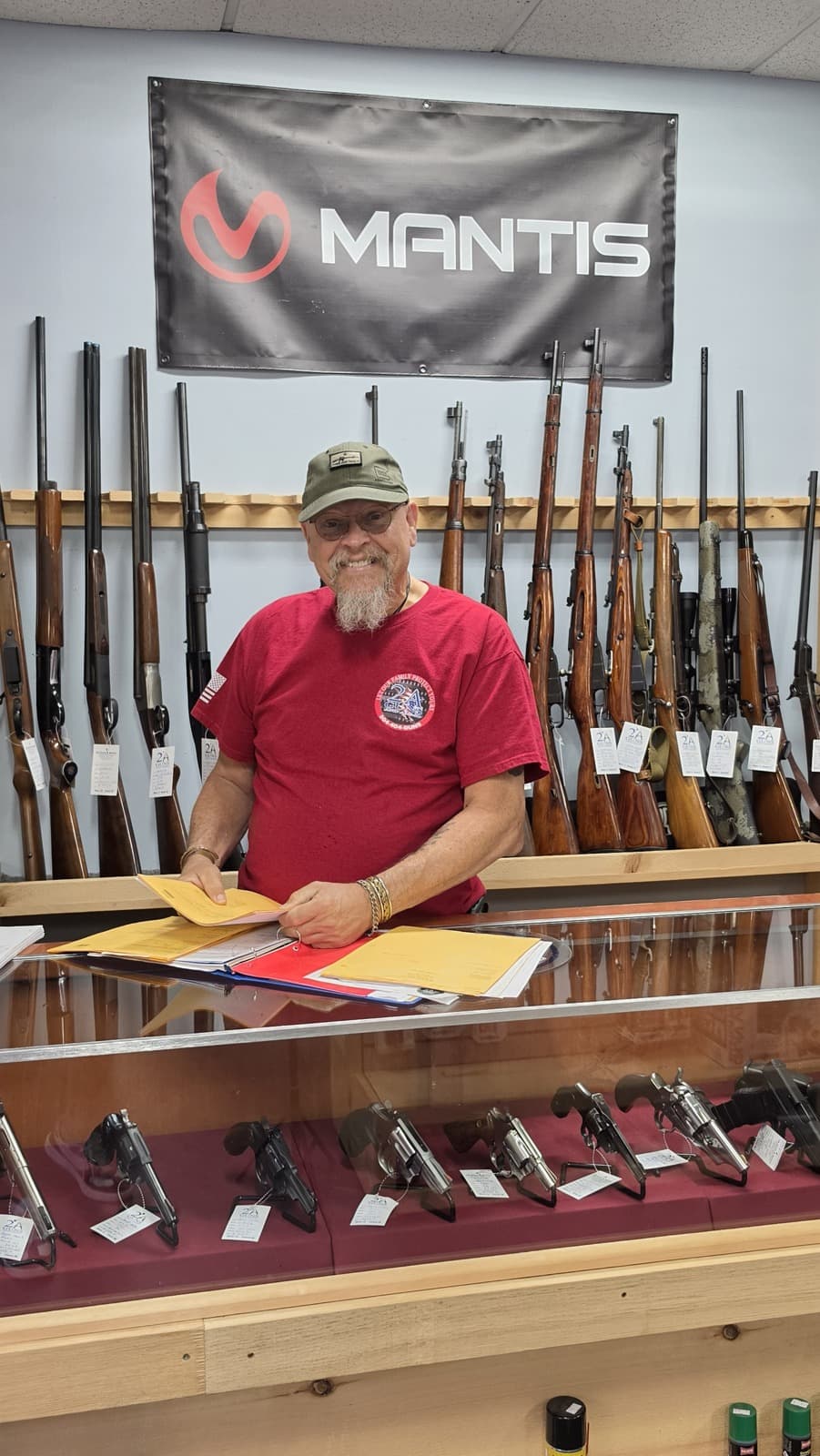 Behind the counter at 2A Guns & Ammo, in front of the long-gun wall